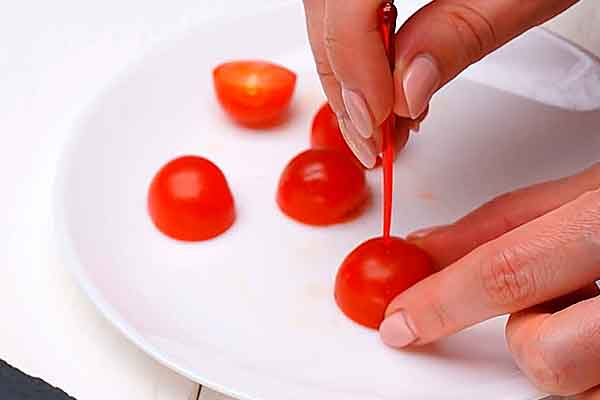 Режем на половинки помидоры, прокалываем по середине пластиковой шпажкой
